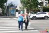 9月18日，在延吉市局子街北大市場西側的十字路口旁，大學志愿者劉書達頭戴志愿者標志帽、身穿藍馬甲、佩戴綬帶和袖標，手拿小紅旗，在路口維護交通秩序，引導行人通過斑馬線安全過馬路。